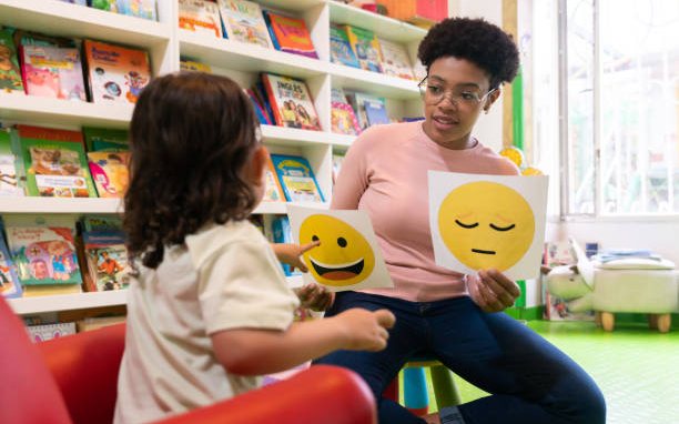 A teacher holding up a happy face card and a sad face card for a toddler during a feelings lesson