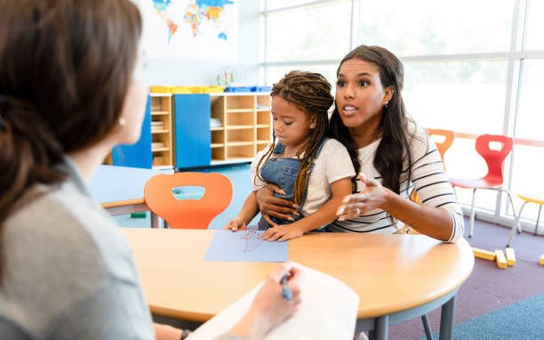 A mother holding her young daughter across the table from a director during an enrollment interview