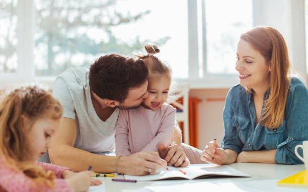 Two parents drawing and writing at a table with their two young children